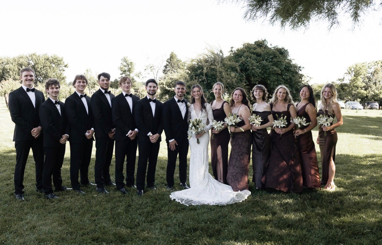 The full bridal party on a lawn, groomsmen in black and bridesmaids in deep brown